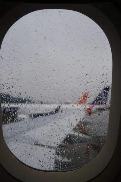 Blurred of wing of airplane see through the rain drop on window of plane that land on the airport in the rainy evening with the cloudy day — Stock Photo, Image