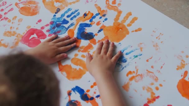 Mała dziewczynka z farbami na rękach rysuje na białym papierze. Widok z góry — Wideo stockowe