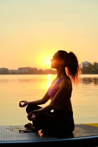 Gün batımında yemek güvertesinde yoga yapan genç bir kadın. Kapat.