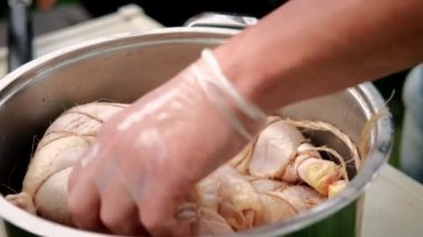 Hands of chef in gloves, take marinated chicken legs for further cooking.