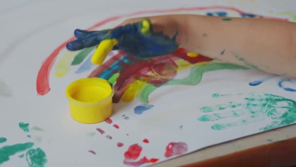 Little girl with paints on her hands draws on white paper. Top view shot. Close up Slow motion — Stock Video
