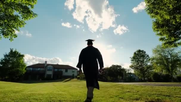 Οπίσθια φωτογραφία του φοιτητή αποφοίτων πανεπιστημίου στο ηλιοβασίλεμα Silhouette πηγαίνει στο δρόμο. Αργή κίνηση στο μέλλον — Αρχείο Βίντεο