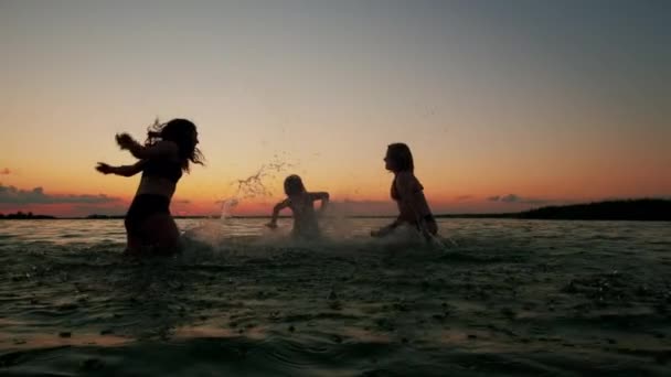 Σιλουέτες παιδιών το ηλιοβασίλεμα μέσα στο νερό της παραλίας. Χαρούμενη φιλική οικογένεια. Αργή κίνηση — Αρχείο Βίντεο