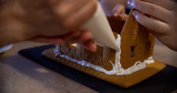 Woman and little girl decorate gingerbread house. Traditional christmas family entertainment. Close up