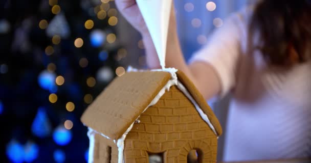 Девушка украшает пряничный домик. Традиционные рождественские семейные развлечения. Закрыть — стоковое видео