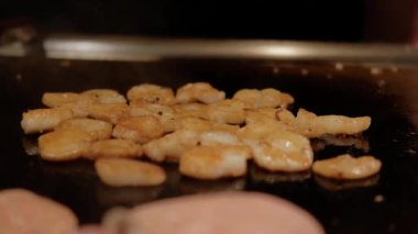 Japon şefin Japon karidesli teppanyaki pişirişini yakından izleyin. Elektrikli ocakta karides kızartıyorlar. Yavaş çekim gelecek