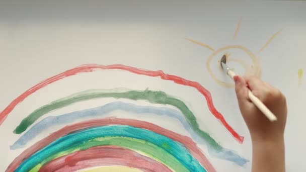 少女は手に筆を持ち、白い紙に彩色した虹を描く。トップビューショット — ストック動画