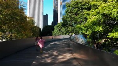Küçük kızlar Chicago 'daki BP yaya köprüsü boyunca modern şehir manzaralı bir binayla yürüyorlar. Şikago İl. ABD 01 Ekim 2025. Yüksek kalite 4k görüntü