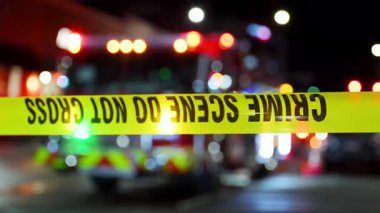 Açık sarı bir olay yeri şeridi şehir ortamında incelenmek üzere yasaklanmış bir bölgeyi işaret ediyor. Arka planda yangın söndürme ışıkları var. Yüksek kalite 4k görüntü