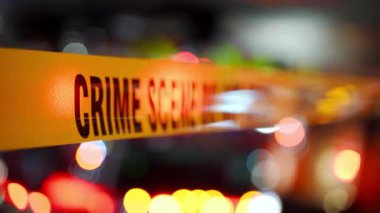 Açık sarı bir olay yeri şeridi şehir ortamında incelenmek üzere yasaklanmış bir bölgeyi işaret ediyor. Arka planda parlayan polis ışıkları var. Yüksek kalite 4k görüntü