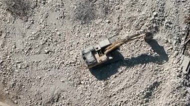 Büyük bir enkaz ve kir alanı üzerinde çalışan bir kazıcı ile yıkım alanı. Zemin molozlarla kaplı, beton veya eski yapının kalıntıları yıkılıyor. Ağır çekim. Yüksek kalite 4k görüntü