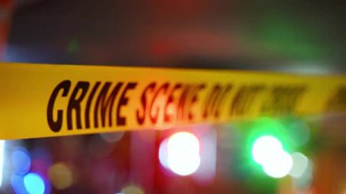 Açık sarı bir olay yeri şeridi şehir ortamında incelenmek üzere yasaklanmış bir bölgeyi işaret ediyor. Arka planda polis ya da kurtarma ekibinin yanıp sönen ışıkları var. Yüksek kalite 4k görüntü