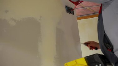 İnşaat işçisi, metal bir bant bıçağıyla elektrik prizi kutusunun yanındaki alçıpan üzerine eklem bileşimi yayıyor. Duvar pürüzsüz ve bitmiş. Yüksek kalite 4k görüntü