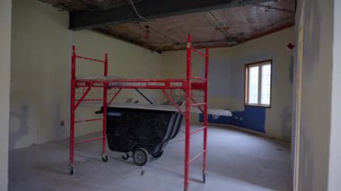 İnşaat iskelesi ve merkeze yerleştirilmiş bir el arabası olan yenilenmiş bir oda. Tavan yalıtımı ve tamamlanmamış alçıpan, tadilatın devam ettiğini gösteriyor. Yüksek kalite 4k görüntü