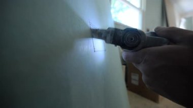 Alçıpandaki dikdörtgen açığı kesmek için salınan çoklu bir alet kullanan bir inşaat işçisinin yakın çekim görüntüsü. Bıçak keserken toz parçacıkları görülebilir. Yüksek kalite 4k görüntü