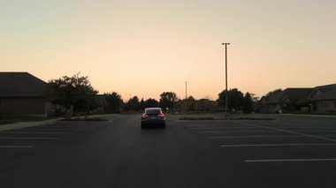 Tesla alacakaranlıkta boş banliyö otoparkından geçiyor. Gökyüzü gün batımının renkleriyle ışıldar, dikiz manzarası. Naperville lL 'de. ABD 2 Eylül 2025. Yüksek kalite 4k görüntü