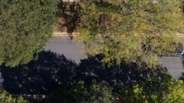 Ağaçlarla kaplı bir banliyö yolunda giden bir Tesla arabasının yukarıdan aşağıya insansız hava aracı görüntüsü. EV, güneş ışığı ve gölgelerin altında sorunsuz hareket eder. ABD Naperville IL 01 Ekim 2025. Yüksek kalite 4k görüntü