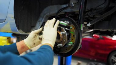 Koruyucu eldivenlerdeki tamirci arabanın tekerlek merkezini ve disk frenlerini tamir eder, araba kaldırılır. Bir tamirhanede çeşitli cihazlar. Yüksek kalite 4k görüntü
