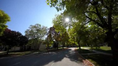 POV güneşli bir yaz ya da sonbahar gününde banliyöde huzurlu bir yolculuk yapar. Yeşil yapraklı ağaçlar caddeyi kaplıyor ve güneş ışığı sıcak ve davetkar bir atmosfer yaratıyor. Yüksek kalite 4k görüntü