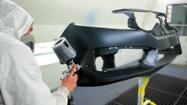 Araba tamponundaki oto teknisyeninin sprey boyasını temiz, havalandırmalı boya kabinine kapatın. Yüksek hassasiyetli sprey tabanca kullanarak koruyucu tulum ve solunum cihazı takıyor. Yüksek kalite 4k görüntü