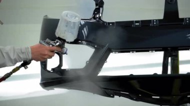 Otomobil teknisyeni, araba tamponuna parlatıcı sürmüş. Temiz, havalandırmalı boya kabini. Yüksek hassasiyetli sprey tabanca kullanarak koruyucu tulum ve solunum cihazı takıyor. Yüksek kalite 4k görüntü