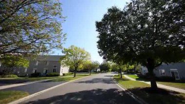 POV güneşli bir yaz ya da sonbahar gününde sakin bir banliyö mahallesinde huzurlu bir şekilde araba sürer. Yeşil yapraklı ağaçlar caddeyi kaplıyor ve güneş ışığı sıcak ve davetkar bir atmosfer yaratıyor. Yüksek kalite 4k görüntü