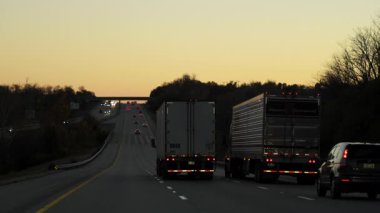 Yarı kamyonlar 25 metrelik yarı karavan römorklarıyla altın gün batımında otoyolda ilerliyorlar. Amerika eyaletleri arası uzun mesafe nakliye aracı. Yüksek kalite 4k görüntü