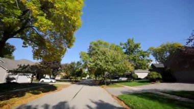 POV güneşli bir yaz veya sonbahar gününde sakin bir banliyö mahallesi boyunca huzurlu bir yolculuk yapar. Yeşil yapraklı ağaçlar caddeyi kaplıyor ve güneş ışığı sıcak ve davetkar bir atmosfer yaratıyor. Yüksek kalite 4k görüntü