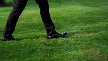 Siyah pantolonlu ve ayakkabılı bir adam parkta yeşil çimlerde yürüyor. Yüksek kalite 4k görüntü