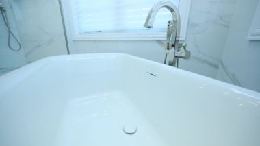 Beyaz entegre banyo lavabosundaki parlak krom musluk parlak, modern bir iç mekandaki parlak tezgahın üzerine kurulmuş. Temiz çizgiler, yansıtıcı yüzeyler, minimalist estetik. Yüksek kalite 4k görüntü
