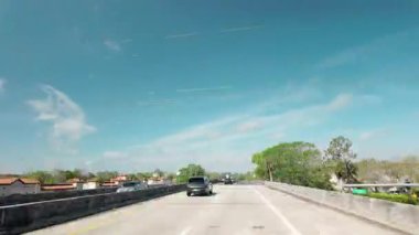 POV, açık mavi bir gökyüzünün altındaki geniş ve yeni asfalt bir otoyolda çekim yapıyor. Asfalt, parlak güneş ışığı, yol işaretleri ve yeşil ağaçlar. Zaman aşımı USA IL Miami 01 Nisan 2025. Yüksek kalite 4k görüntü