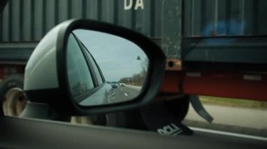 Kamyonun yansıması, bahar günü yolda giden arabanın yan aynasında. Ön yolcu koltuğundan bak. Bulutlar aynada. Yüksek kalite 4k görüntü