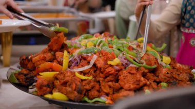 Açık büfede baharatlı tavuk ve dilimlenmiş biber ile soğan karışımı. Tabak canlı, buharlı ve elleri maşa kullanan şenlikli bir ortamda sunuluyor. Yüksek kalite 4k görüntü