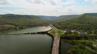 Bereketli yeşil tepelerle çevrili sakin nehir boyunca uzanan uzun otoban köprüsü. Yumuşak bahar renkleri ve parçalı bulutlu bir gökyüzünün altında huzurlu bir doğal atmosfer. Yüksek kalite 4k görüntü