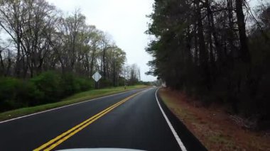 Çevresi ilkbahar ağaçları ve yoğun yeşilliklerle çevrili, yeni döşenmiş kırsal bir yol boyunca sürüş görüntüsü. Virajlı yol, bulutlu gökyüzü ve sessiz orman manzarası. Yüksek kalite 4k görüntü