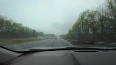 Yağmurlu bir otoyol boyunca giden bir arabanın içinden. Cam silecekleri sisli, bulutlu hava görüşü azalttığı için camda hareket ediyor. USA IL 'de. Naperville 20 Nisan 2025 Yüksek kalite 4K görüntü