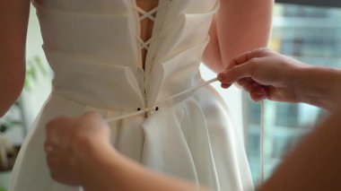 Gelinlik bağlanıyor ve ayarlanıyor. Zarafet ve detaylarla dolu hassas ve samimi bir düğün hazırlığı anı yakalıyor. Yüksek kalite 4k görüntü