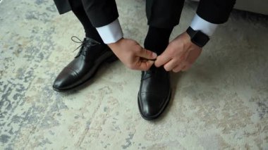 Damat, hazırlanırken resmi siyah ayakkabılarının bağcıklarını bağlıyor, sakin ve zarif bir düğün hazırlığı anı yakalıyor. Yüksek kalite 4k görüntü