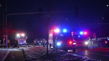Gece vakti çoklu acil durum araçları yanıp sönen ışıklarla kesişen bir kavşakta olay yerine gidiyor. Polis arabaları, itfaiye araçları, ambulanslar, kırmızı ışıkta duran arabalar. Yüksek kalite 4k görüntü