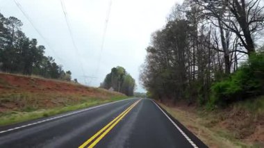 Çevresi ilkbahar ağaçları ve yoğun yeşilliklerle çevrili, yeni döşenmiş kırsal bir yolda sürüş görüntüsü. Virajlı yol, bulutlu gökyüzü ve sessiz orman manzarası. Yüksek kalite 4k görüntü
