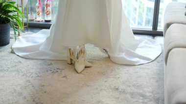 Gelinliğin altına yerleştirilmiş zarif beyaz topuklu gelinlik, içeride yumuşak ve romantik bir hazırlık anı yakalıyor. Yüksek kalite 4k görüntü