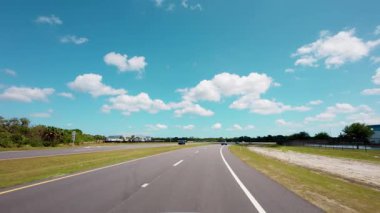 Açık mavi gökyüzü altındaki bir bahar otobanı üzerindeki POV sürüş görüntüsü, sakin bir kırsal alanda pürüzsüz bir trafik ve açık yol manzarası yakalıyor.