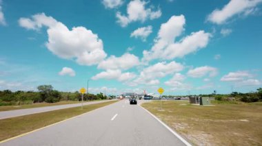 POV, güneşli bir günde Kennedy Uzay Merkezi Ziyaretçi Kompleksi girişine doğru gidiyor. İkonik geçidi ve açık gökyüzünü gösteriyor. USA IL Miami 01 Nisan 2025. Yüksek kalite 4k görüntü