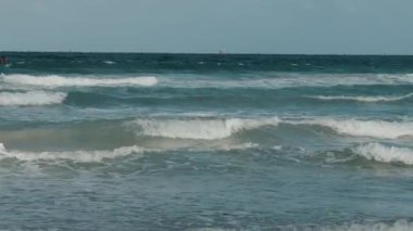 Güneşli bir günde okyanus dalgaları kıyıya doğru yuvarlanıyor, katmanlı dalgalar ve huzurlu mavi sular rahatlatıcı bir sahil manzarası yaratıyor. Yüksek kalite 4k görüntü