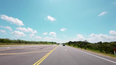 POV, açık mavi gökyüzünün altındaki bir bahar otobanında, huzurlu bir kırsal alanda, pürüzsüz bir trafik ve açık yol manzarası görüntüsü yakalıyor.