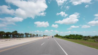 POV, açık mavi bir gökyüzünün altındaki sahil otobanında araç sürüyor. Yol ve inşaat işaretleri, yeşil ağaçlar. Yüksek kalite 4k görüntü