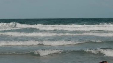 Sakin okyanus dalgaları güneşli bir günde kıyıya doğru yuvarlanıyor, katmanlı dalgalar ve huzurlu mavi sular rahatlatıcı bir sahil manzarası yaratıyor. Yüksek kalite 4k görüntü