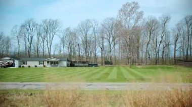 Banliyö evleri ve hareket halindeki bir arabadan yapraksız ağaçlar, açık çimenli ve bahar sonu veya sonbahar sonu atmosferli sakin bir mahalle manzarası gösteriyor. POV görünümü. Yüksek kalite 4k görüntü