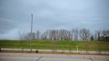 Hareketli bir arabadan çekilen yapraksız ağaçlar ve açık alanlar, sonbahar sonu veya ilkbahar başlarında sessiz renkler ve sakin kırsal atmosferli kırsal manzarayı gösteriyor. POV görünümü. Yüksek kalite 4k görüntü