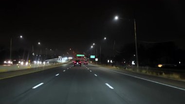 Gece bir otobanda parlayan farları ve stop lambalarıyla dolaşan birden fazla araba görüntüsü. Sahne şehir ulaşımını, gece trafiğini gösteriyor.